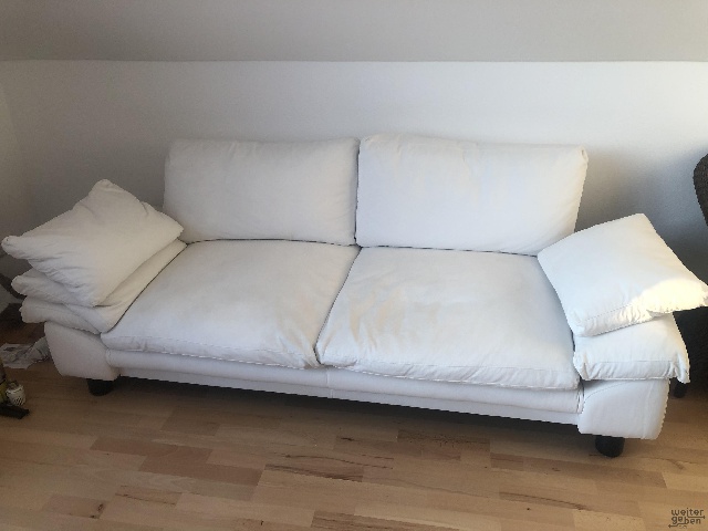 zu sehen: weises zweisitzer Sofa mit großen Rückenlehnen und links und rechts großen Kissen